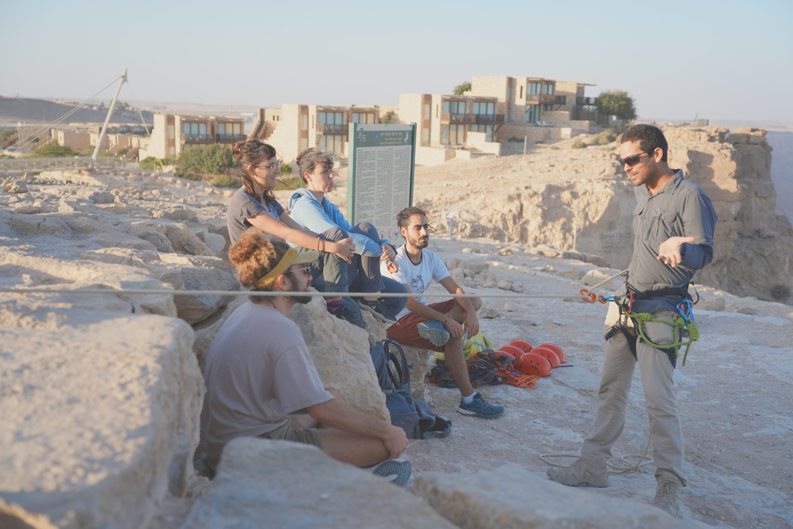 נעם מדריך סנפלינג מדגים לקבוצת אנשים שיושבים על מצוק מכתש רמון